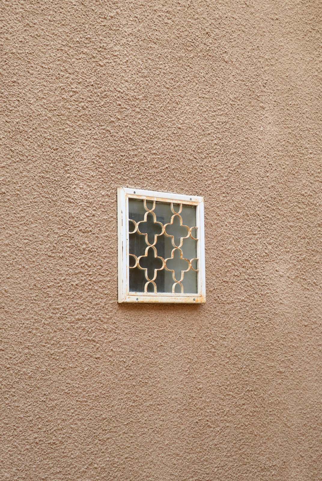 Beige bepleisterde muur met een klein raam met sierrooster