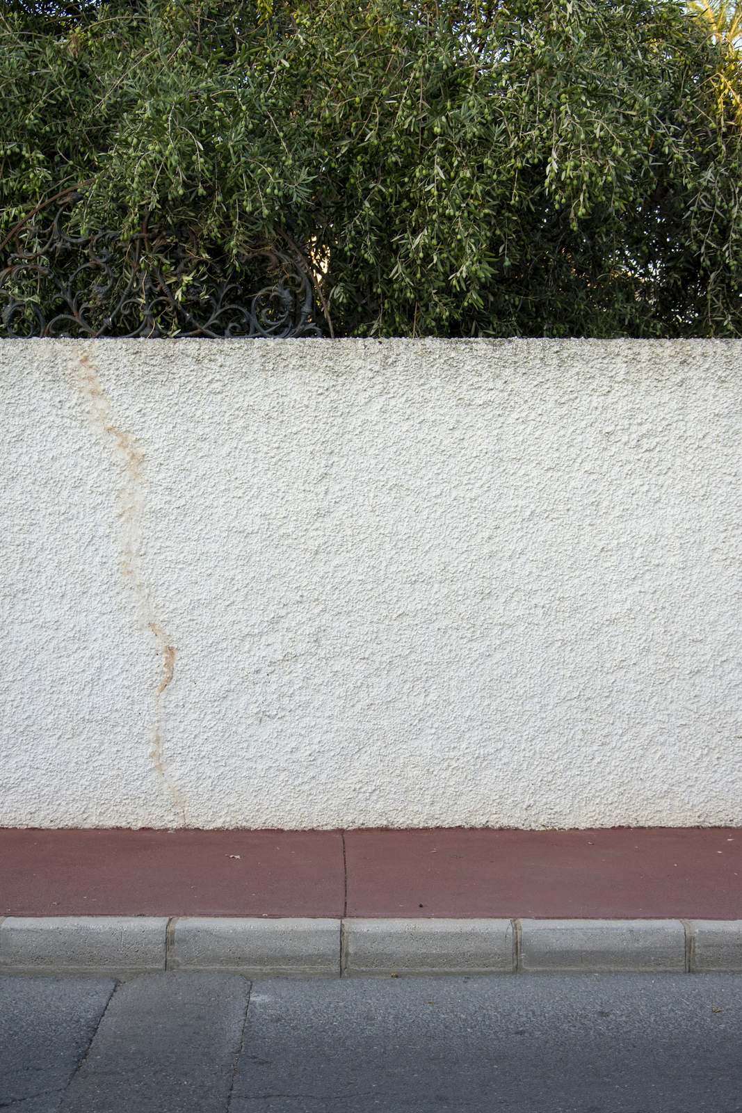 Witte bepleisterde tuinmuur met een roestspoor, boven een roodbruine strook langs de stoep
